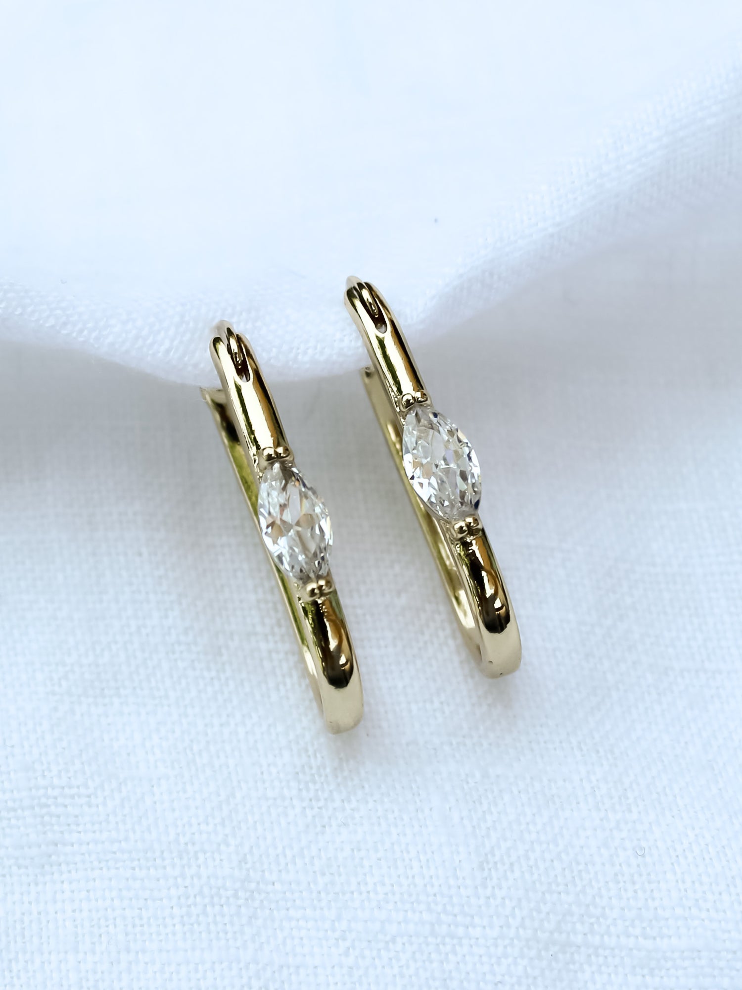 The Ragan Huggie by Kinsey Designs Archives features gold filled hoop earrings with round cubic zirconia gemstones, 1" long, displayed on a white fabric background.