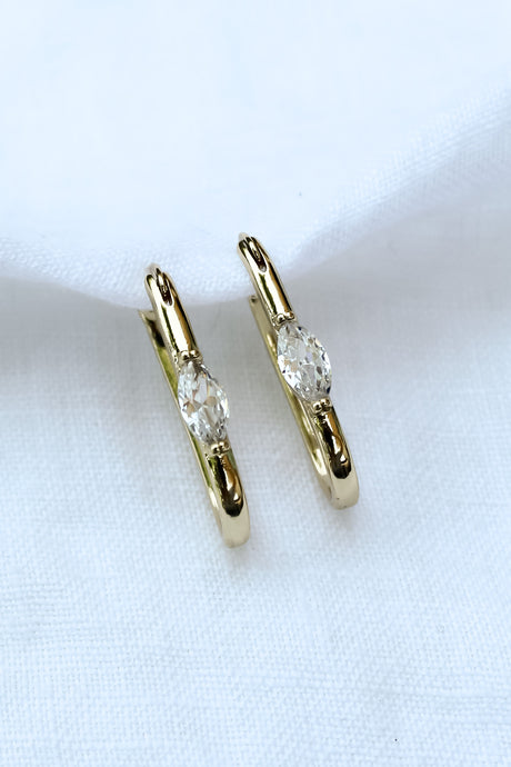 The Ragan Huggie by Kinsey Designs Archives features gold filled hoop earrings with round cubic zirconia gemstones, 1" long, displayed on a white fabric background.