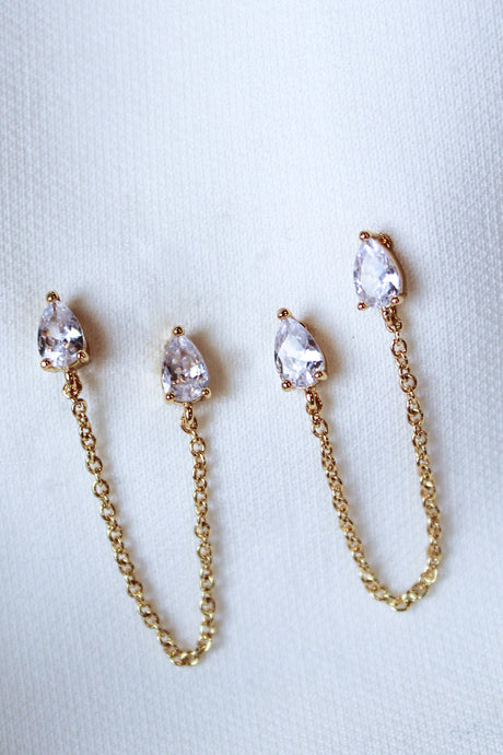The Rayna Post by Kinsey Designs Archives are gold plated chain earrings with teardrop-shaped cubic zirconia, elegantly shown on a white fabric background.