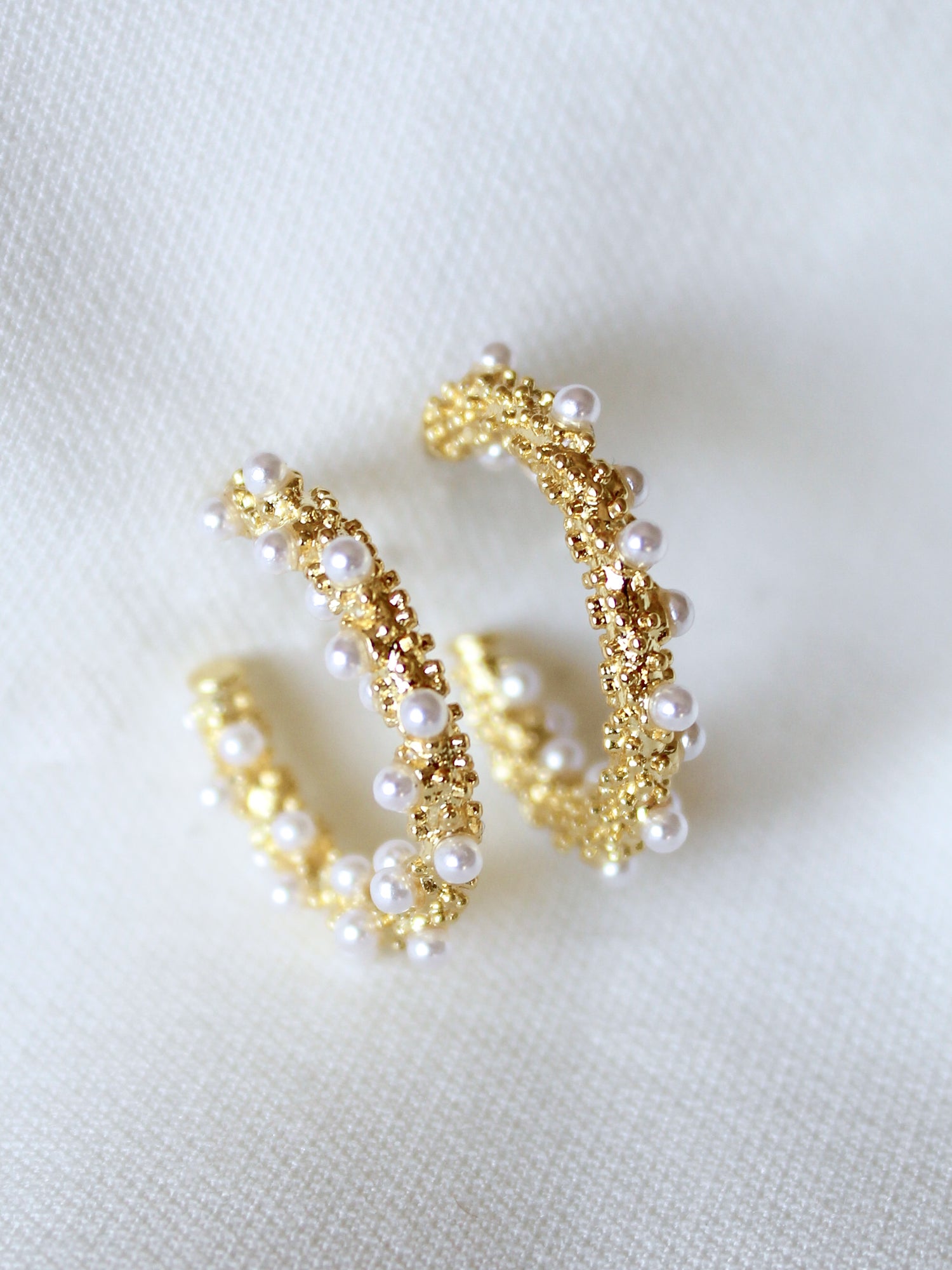 The Reef Hoop by Kinsey Designs Archives features gold hoops with small white pearls, 2" in diameter, displayed on a soft white fabric background.