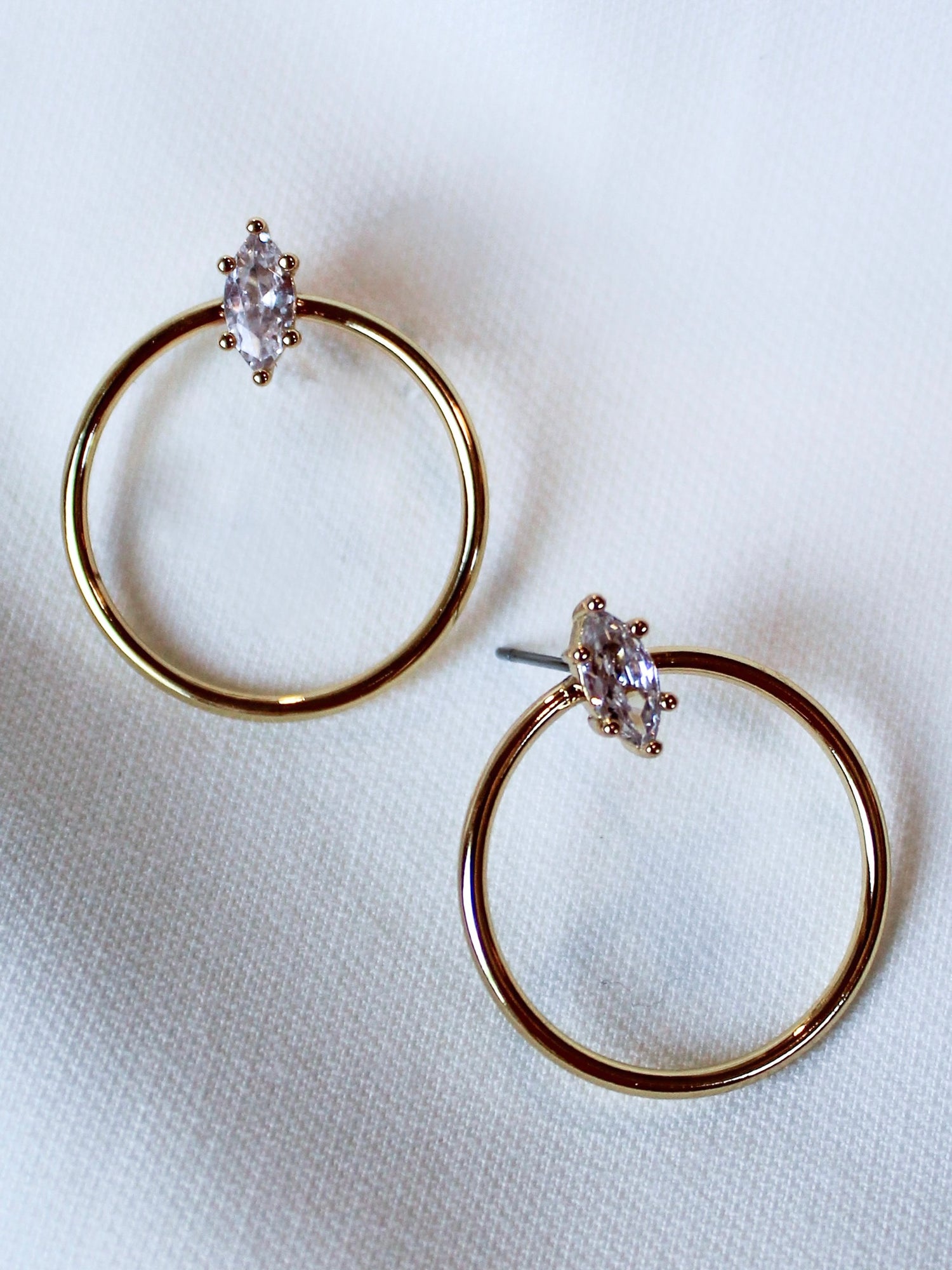 The Remi Hoop by Kinsey Designs Archives features 14K gold plating and marquise-cut cubic zirconia stones. These 1” diameter hoop earrings are shown on a white fabric background.