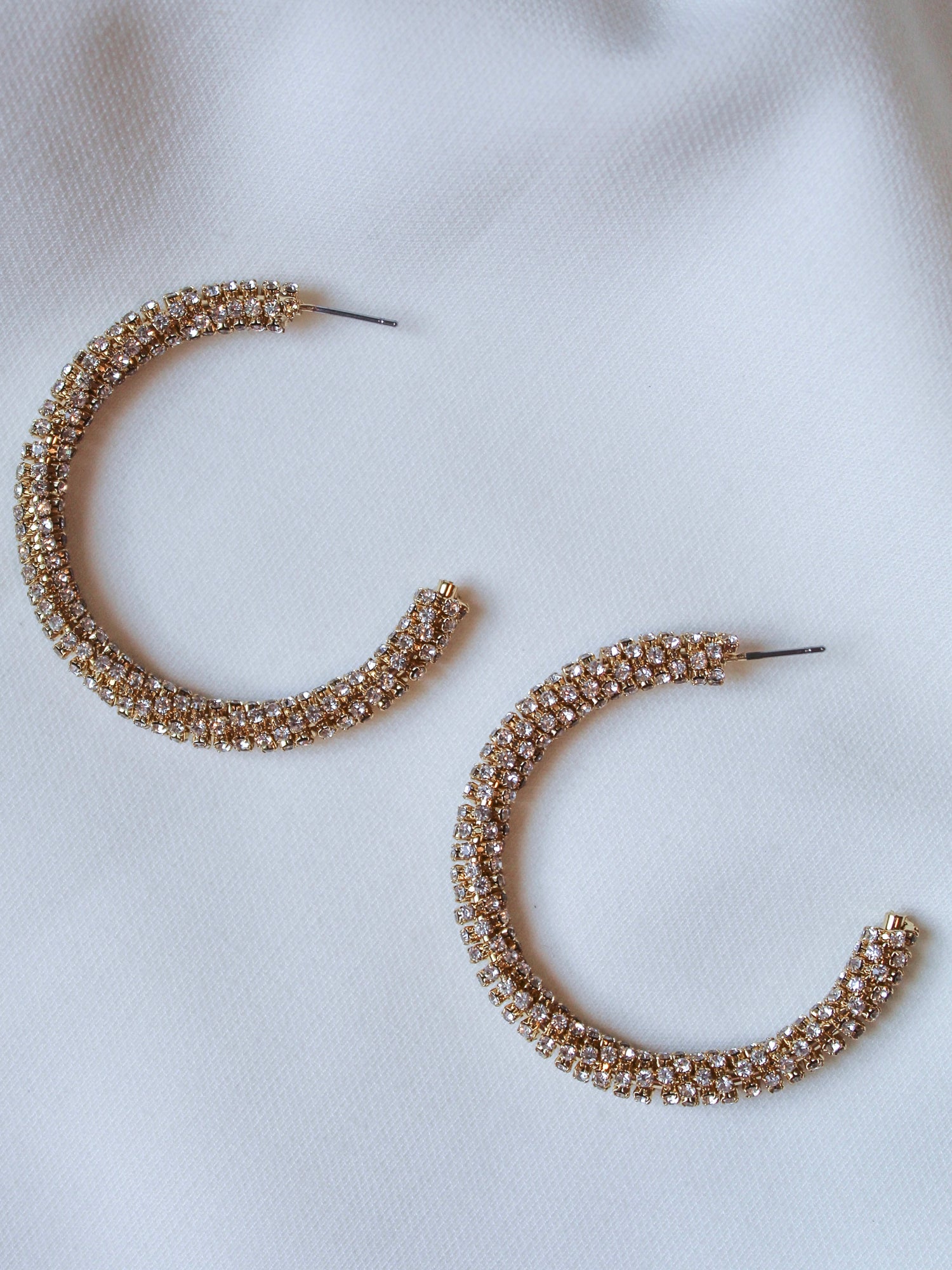 The Kinsey Designs Riley Hoop features gold-plated hoops with embedded cubic zirconia, displayed on a white fabric background—an ideal sample sale find.