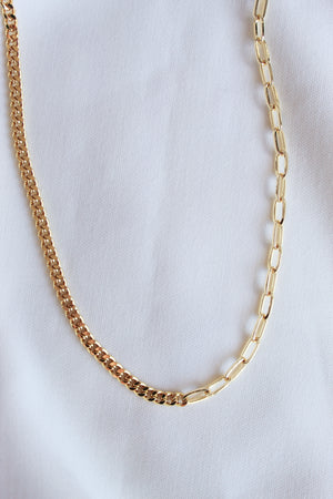 The Saxon Necklace by Kinsey Designs Archives, featuring two gold chains with distinct link styles including a bold chain, is displayed on a white fabric background.
