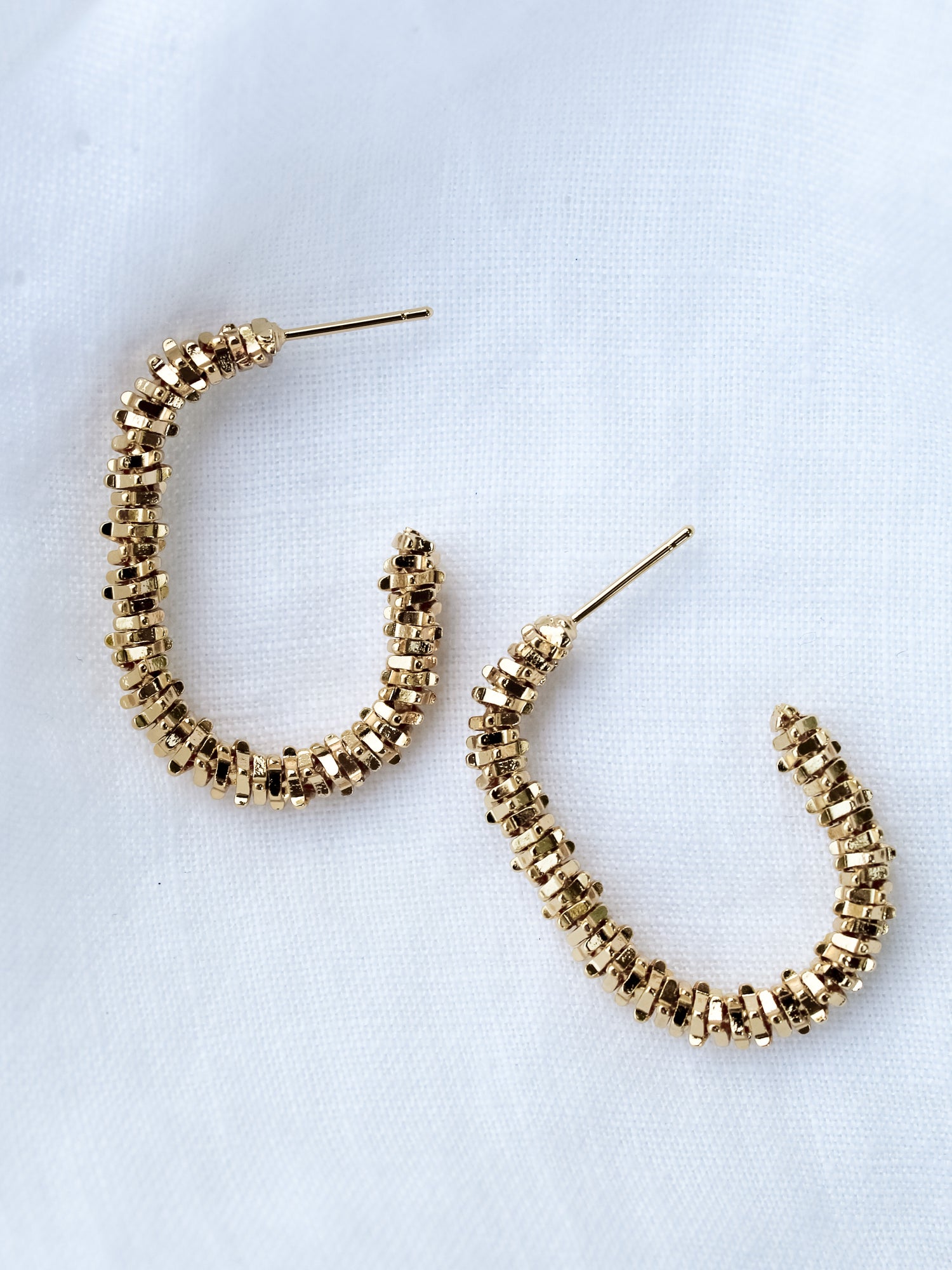 The Shea Hoop by Kinsey Designs Archives: gold plated textured hoops, .75" wide and 1.25" long, shown on a white fabric background.