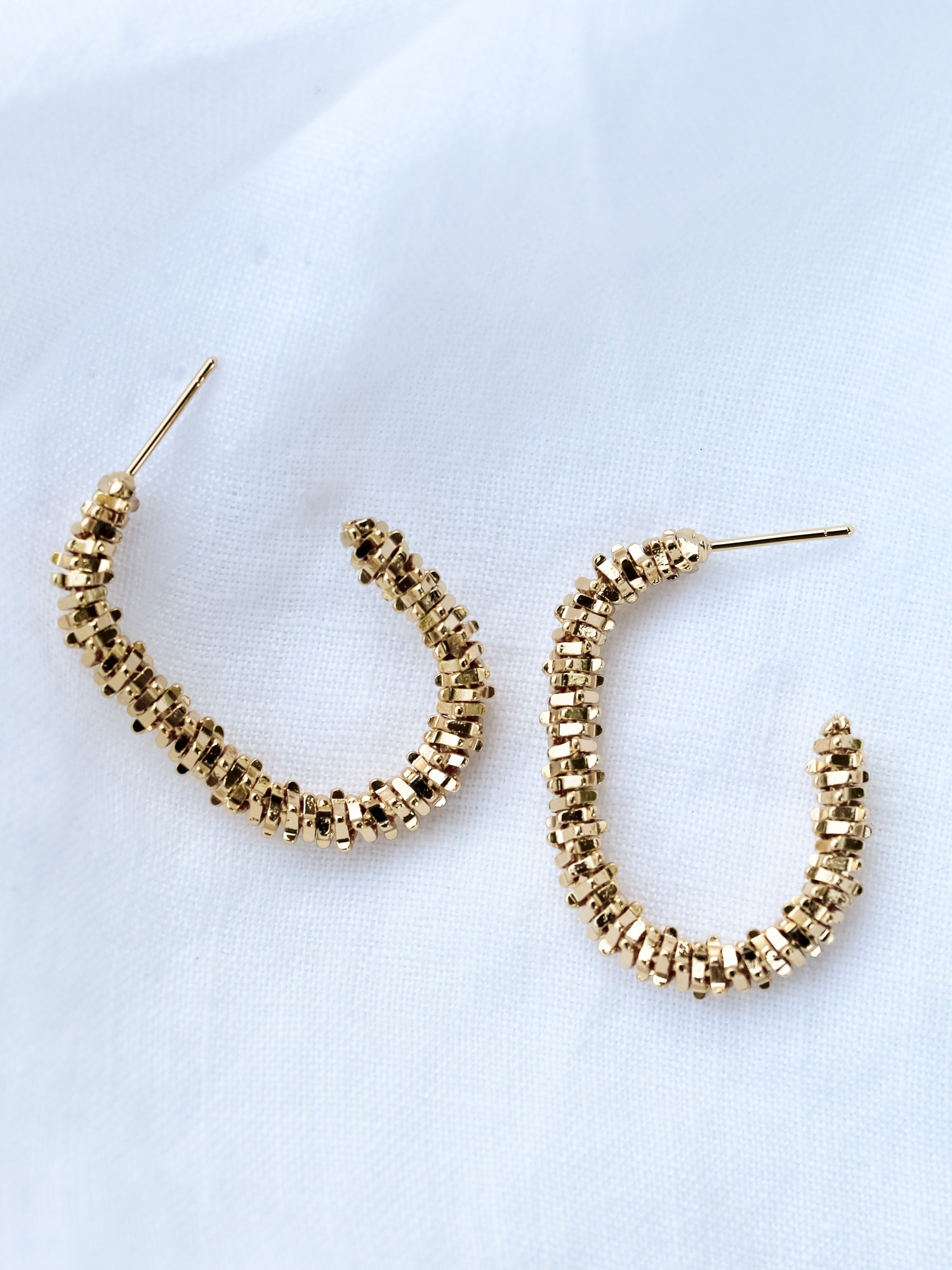 The Shea Hoop by Kinsey Designs Archives features gold plated, textured beaded hoops measuring 1.25" long, displayed on a white fabric background.