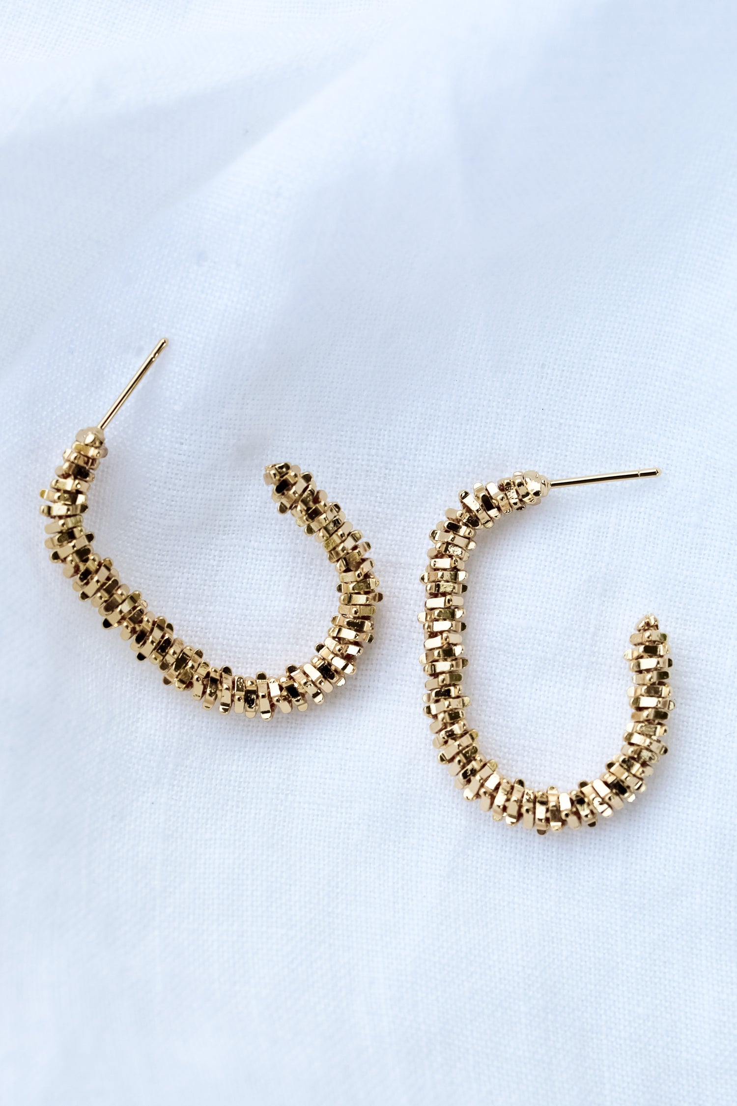 The Shea Hoop by Kinsey Designs Archives features gold plated, textured beaded hoops measuring 1.25" long, displayed on a white fabric background.