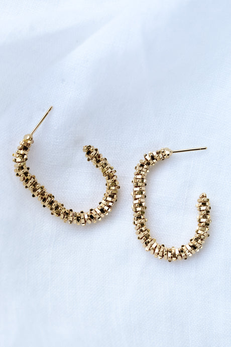 The Shea Hoop by Kinsey Designs Archives features gold plated, textured beaded hoops measuring 1.25" long, displayed on a white fabric background.
