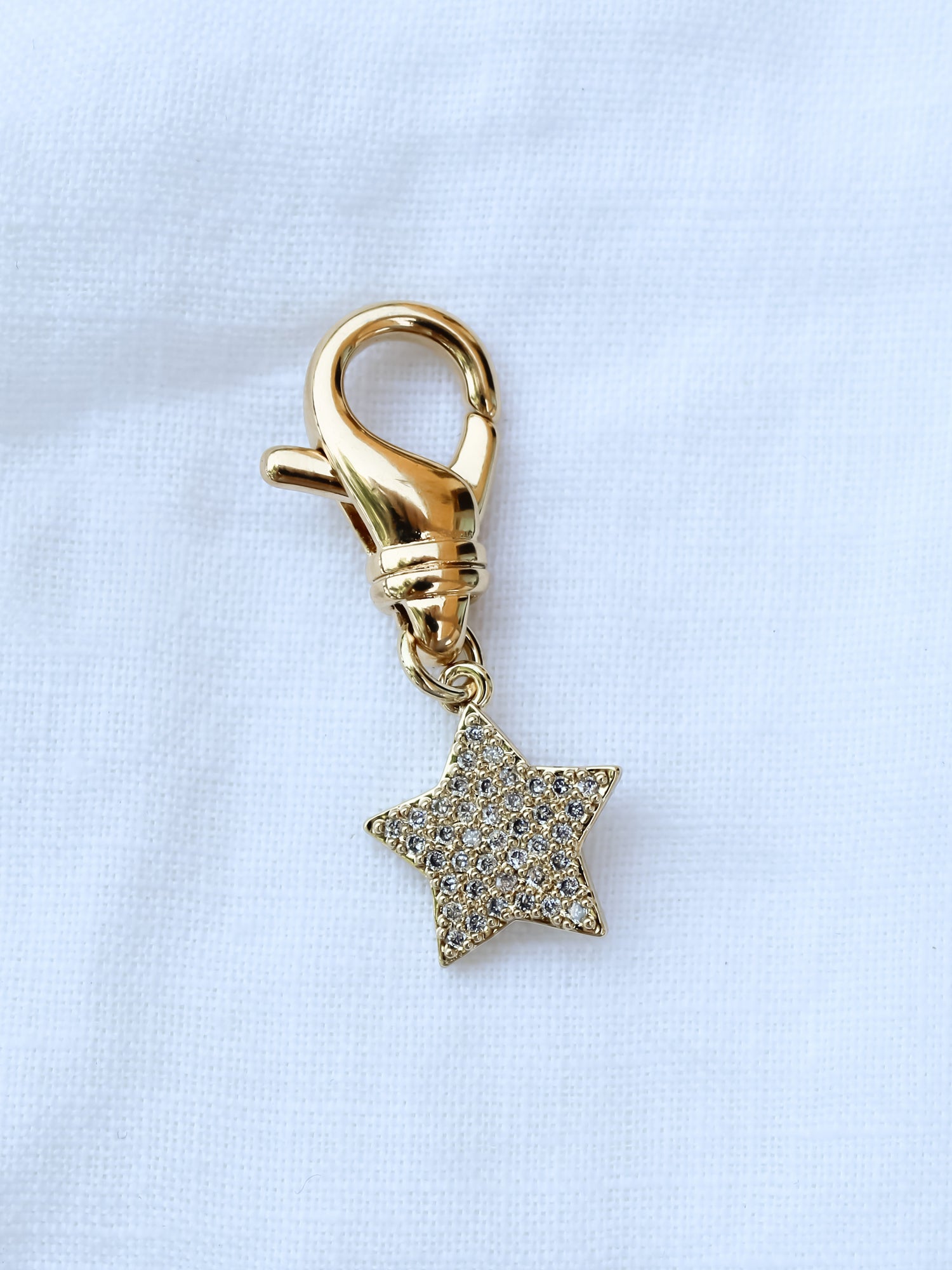 The Star Shoe Charm by Kinsey Designs Archives features a gold-filled clasp with a small, glittery star, displayed on white fabric. Ideal for sample sales or final sale collections.