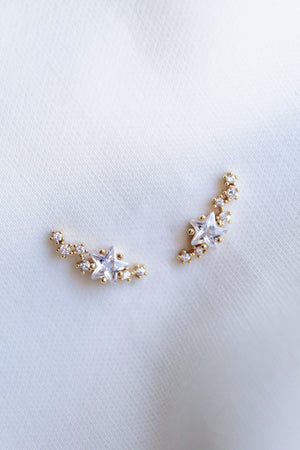 The Kinsey Designs Starlette Climber earrings, featuring star-shaped crystals and sparkling cubic zirconia, are displayed on a soft white fabric background.