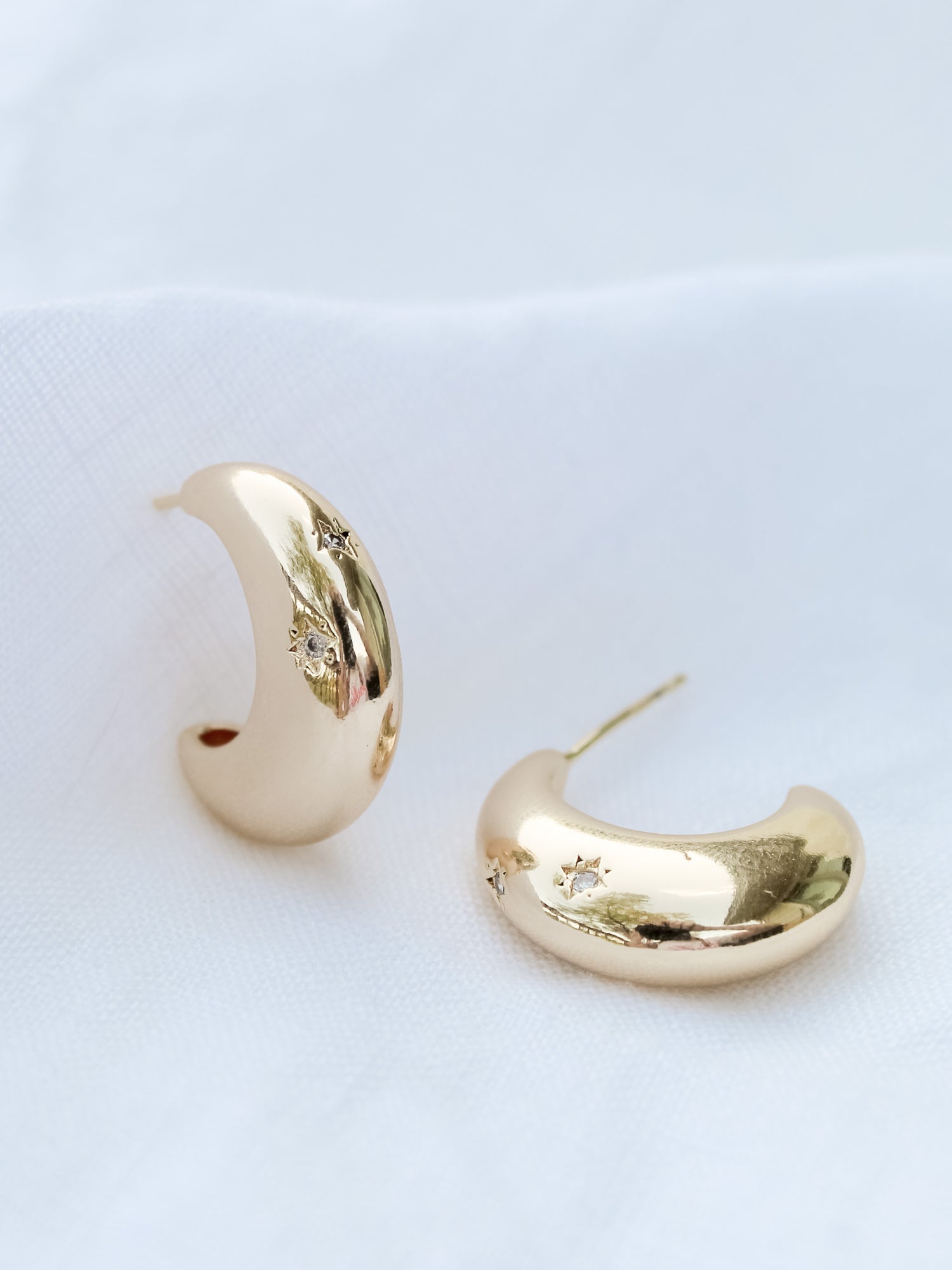 The Swen Earring by Kinsey Designs Archives features .75" wide gold hoops with small star-shaped cubic zirconia, shown on a white fabric background.