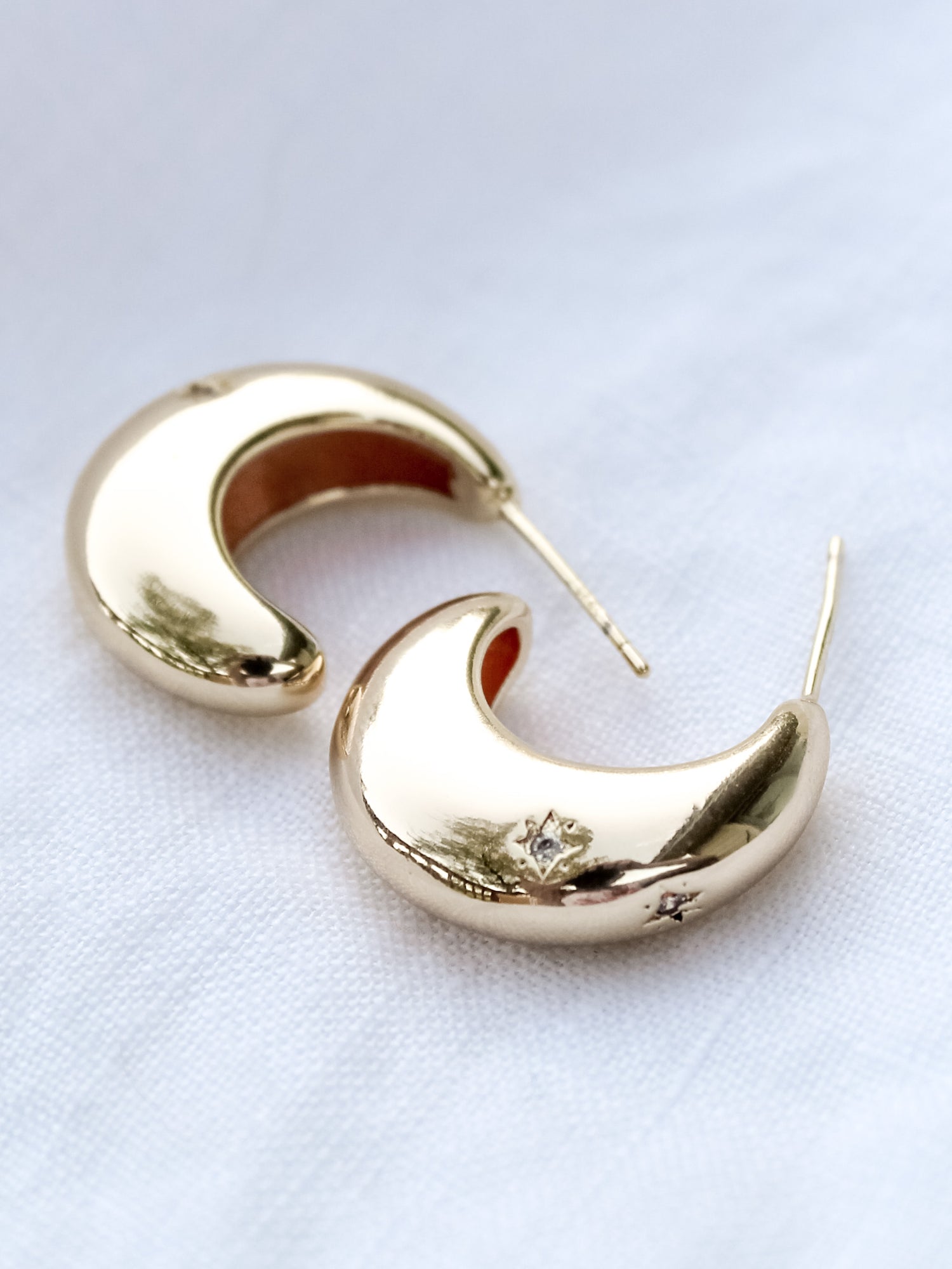 The Swen Earring by Kinsey Designs Archives features a .75" wide crescent shape in 14k gold fill, sparkling with cubic zirconia, shown on a white fabric background.