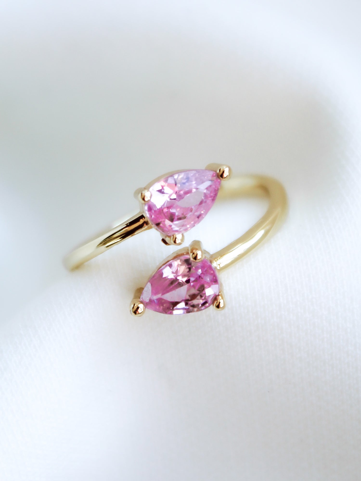 The Teara Ring Pink Ice by Kinsey Designs Archives features two pear-shaped pink cubic zirconia stones, beautifully displayed on a soft white fabric background.