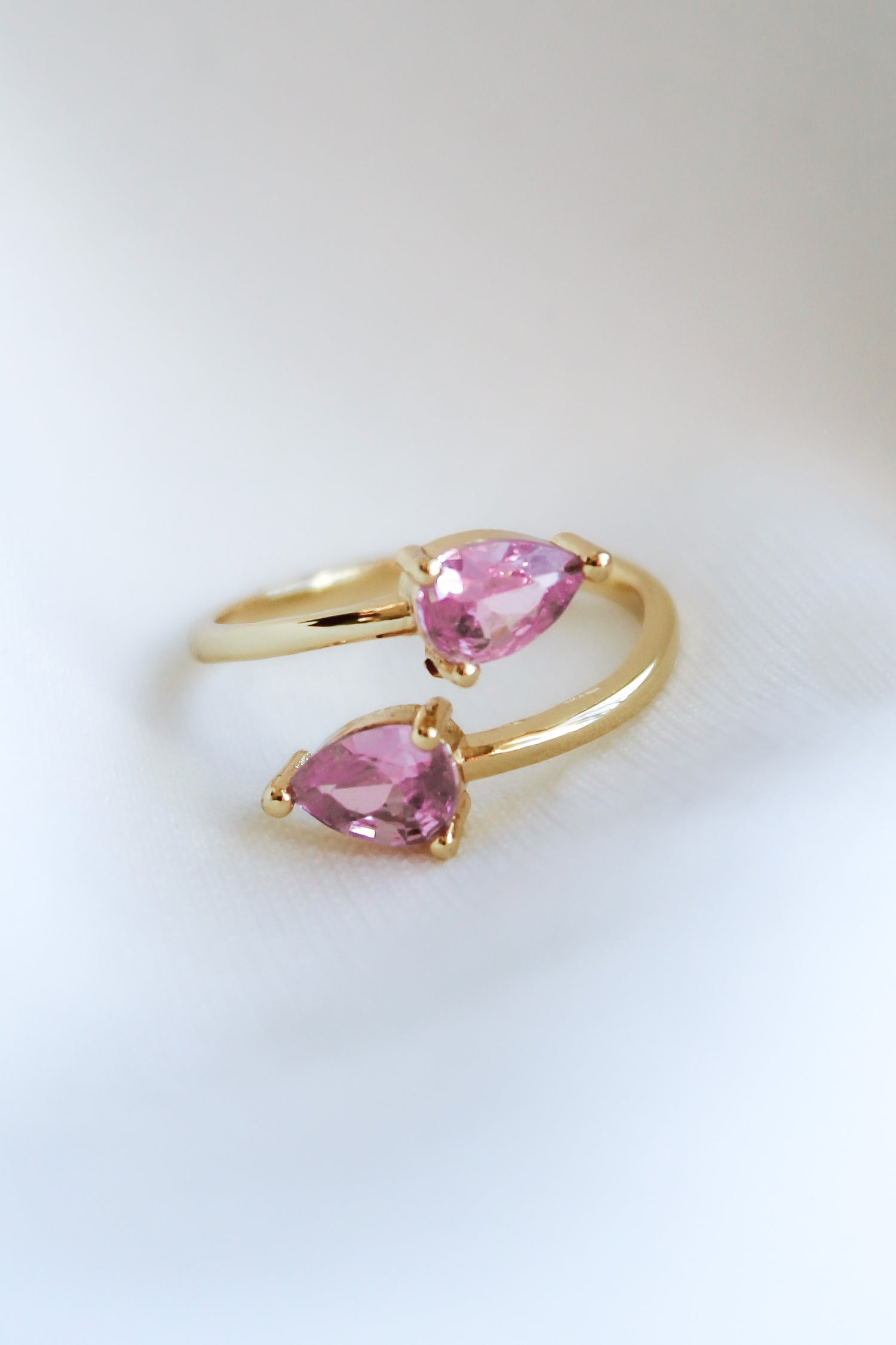 The Teara Ring Pink Ice by Kinsey Designs Archives, featuring two pear-shaped pink cubic zirconia stones, sparkles against a soft white background.