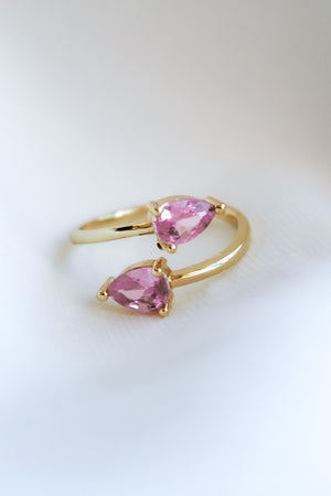 The Teara Ring Pink Ice by Kinsey Designs Archives, featuring two pear-shaped pink cubic zirconia stones, sparkles against a soft white background.
