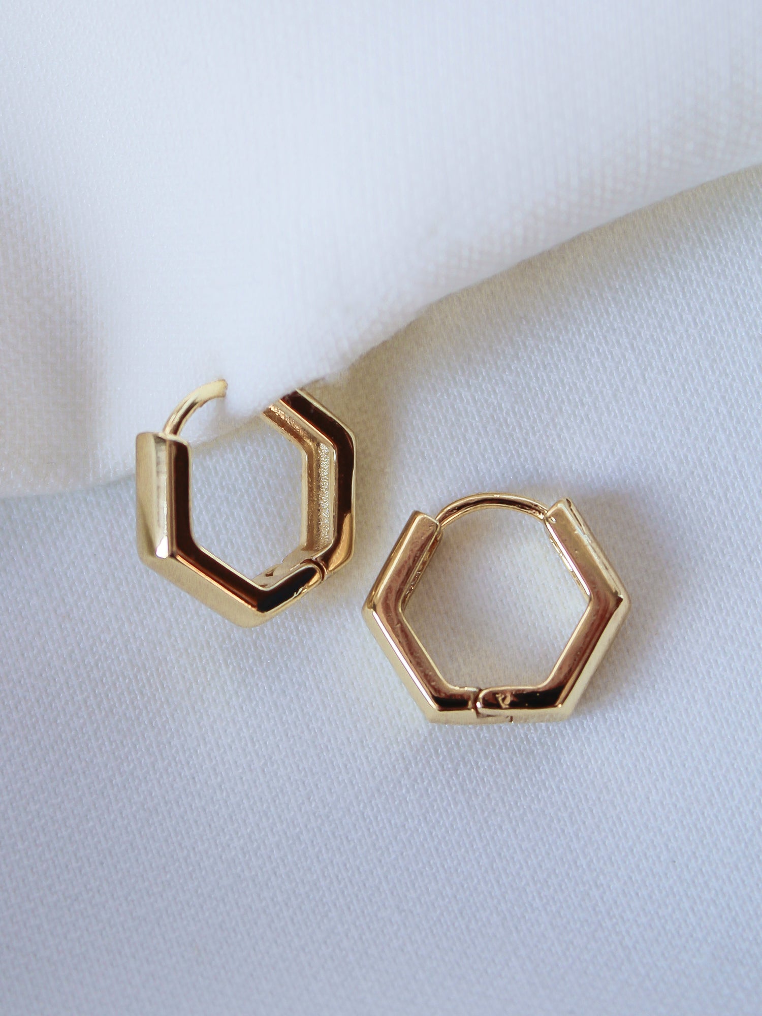 The Theo Hoop by Kinsey Designs Archives—gold filled, hexagon-shaped earrings—rests on white fabric. A modern touch for any look, these earrings are part of our final sale.