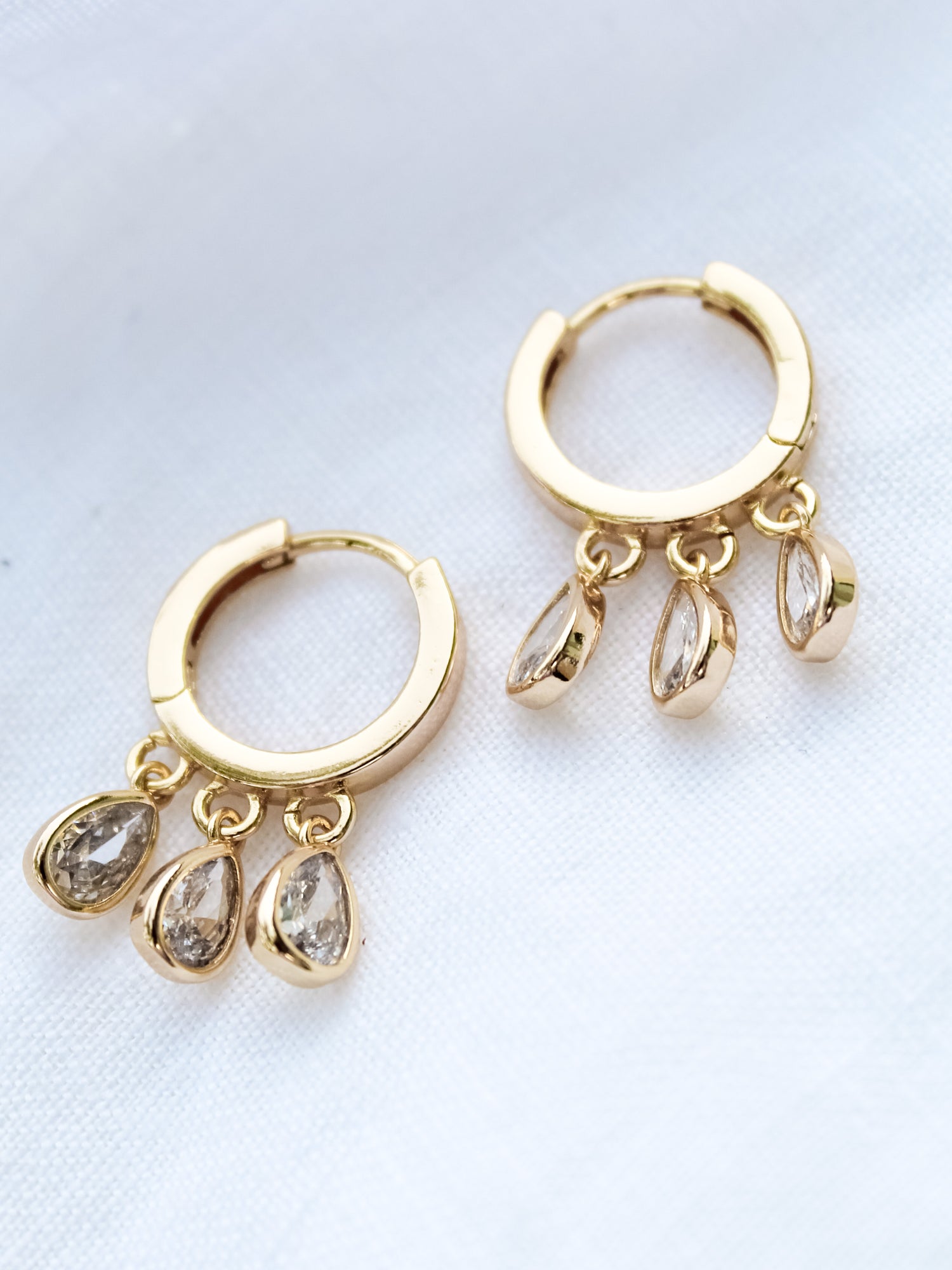 The Tove Huggie by Kinsey Designs Archives features 1-inch gold filled hoops with three teardrop-shaped cubic zirconia charms, shown on white fabric.
