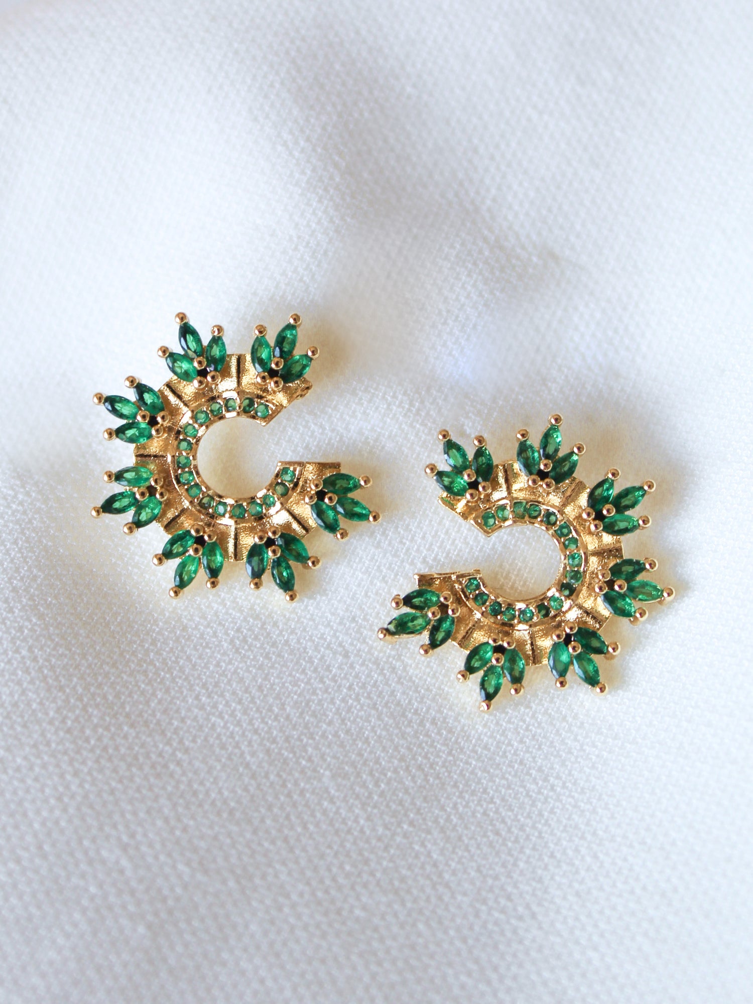 The Vina Stud earrings by Kinsey Designs Archives feature green stones in a circular sunburst design, set in gold fill, displayed on white fabric; each earring measures 0.65 inches in diameter.