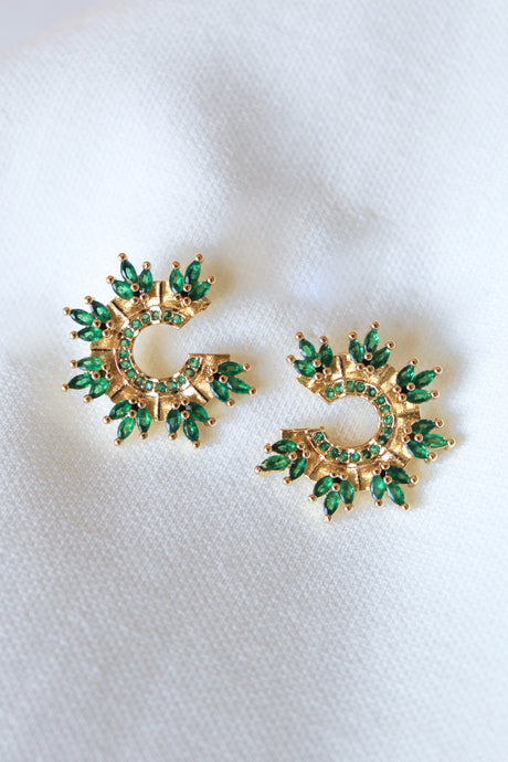 The Vina Stud earrings by Kinsey Designs Archives feature green stones in a circular sunburst design, set in gold fill, displayed on white fabric; each earring measures 0.65 inches in diameter.