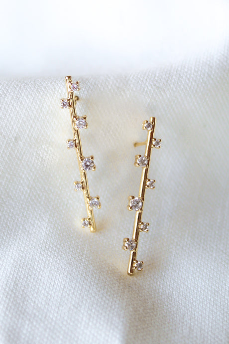 The Walker Earring by Kinsey Designs Archives features 1.5-inch gold-filled drops with vertical rows of small cubic zirconia, shown on a white fabric background. These elegant earrings bring subtle sparkle to any look.