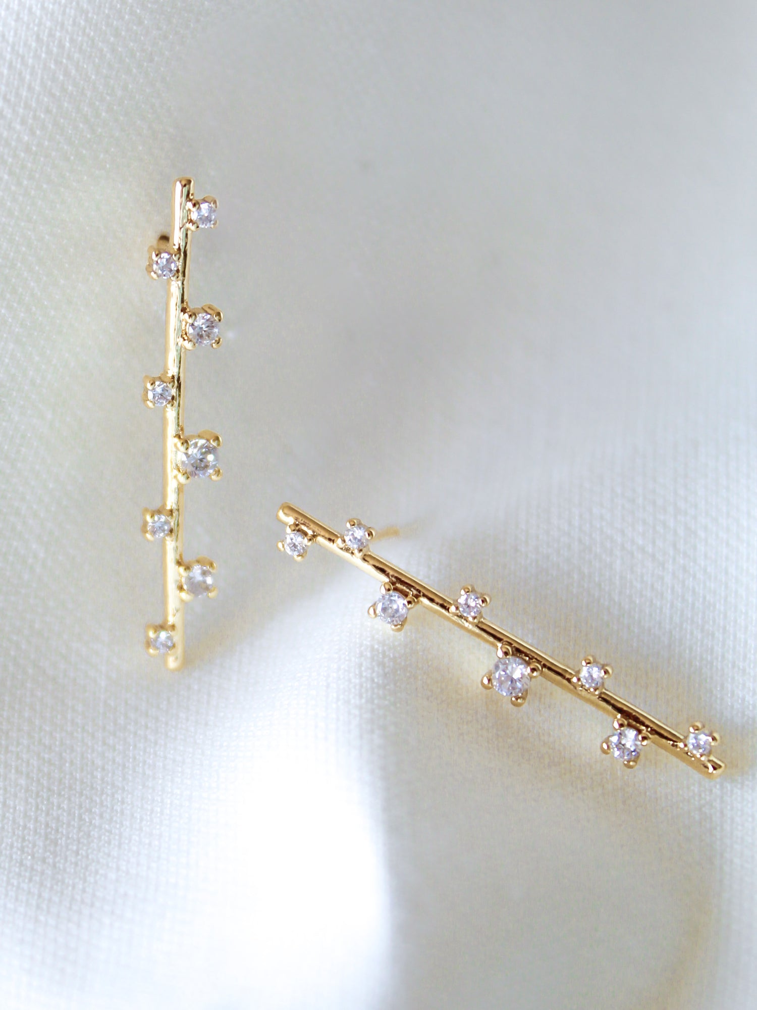 The Walker Earring by Kinsey Designs Archives features a sleek bar design with sparkling cubic zirconia, displayed on soft white satin fabric.