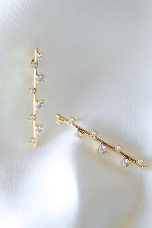 The Walker Earring by Kinsey Designs Archives features a sleek bar design with sparkling cubic zirconia, displayed on soft white satin fabric.