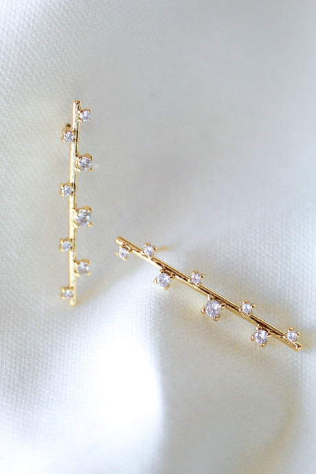 The Walker Earring by Kinsey Designs Archives features a sleek bar design with sparkling cubic zirconia, displayed on soft white satin fabric.