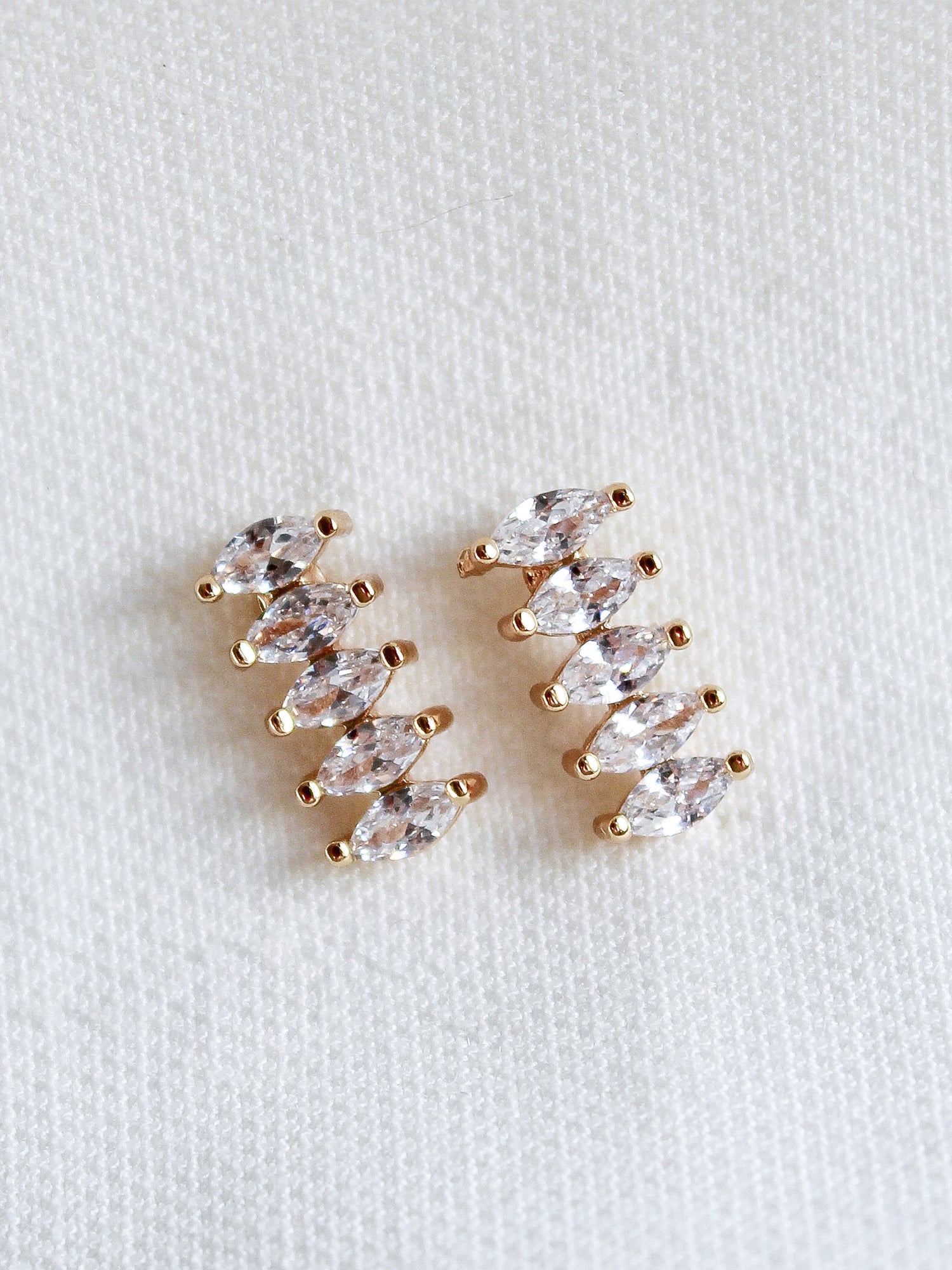 The Winnie Post earrings by Kinsey Designs Archives feature five marquise-cut cubic zirconia stones each, set in gold fill and displayed on a white textured fabric background.