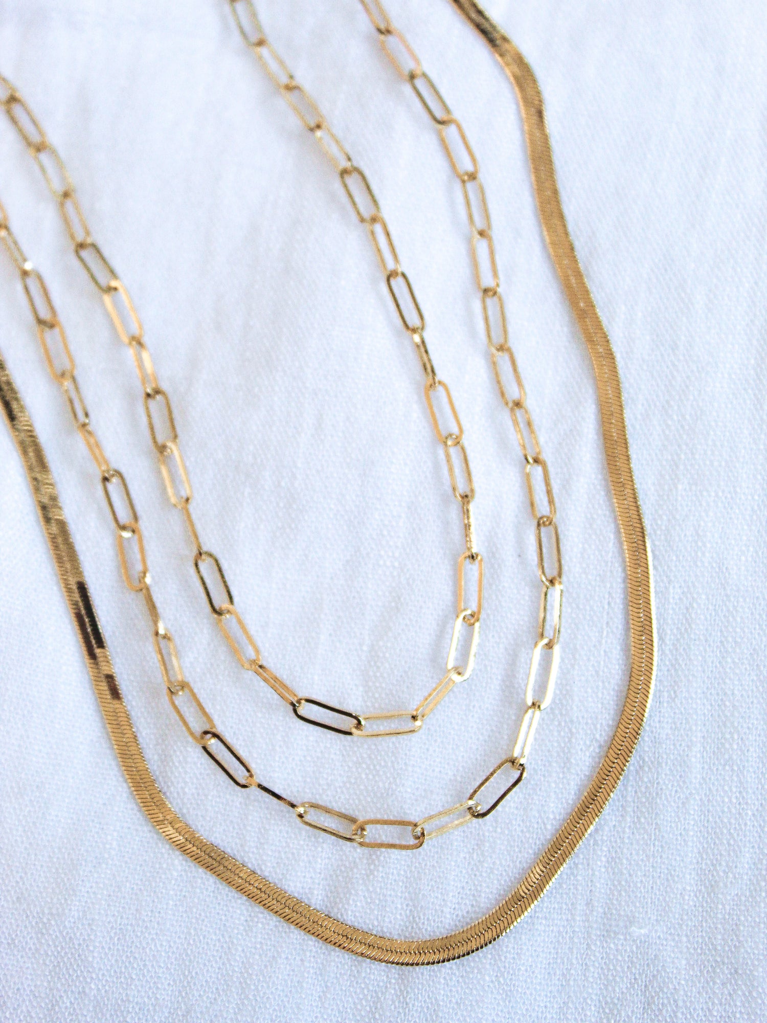 The Wren Chain Layer by Kinsey Designs Archives features three 16k gold plated chains with varying link styles, elegantly layered together and displayed on a white fabric background.