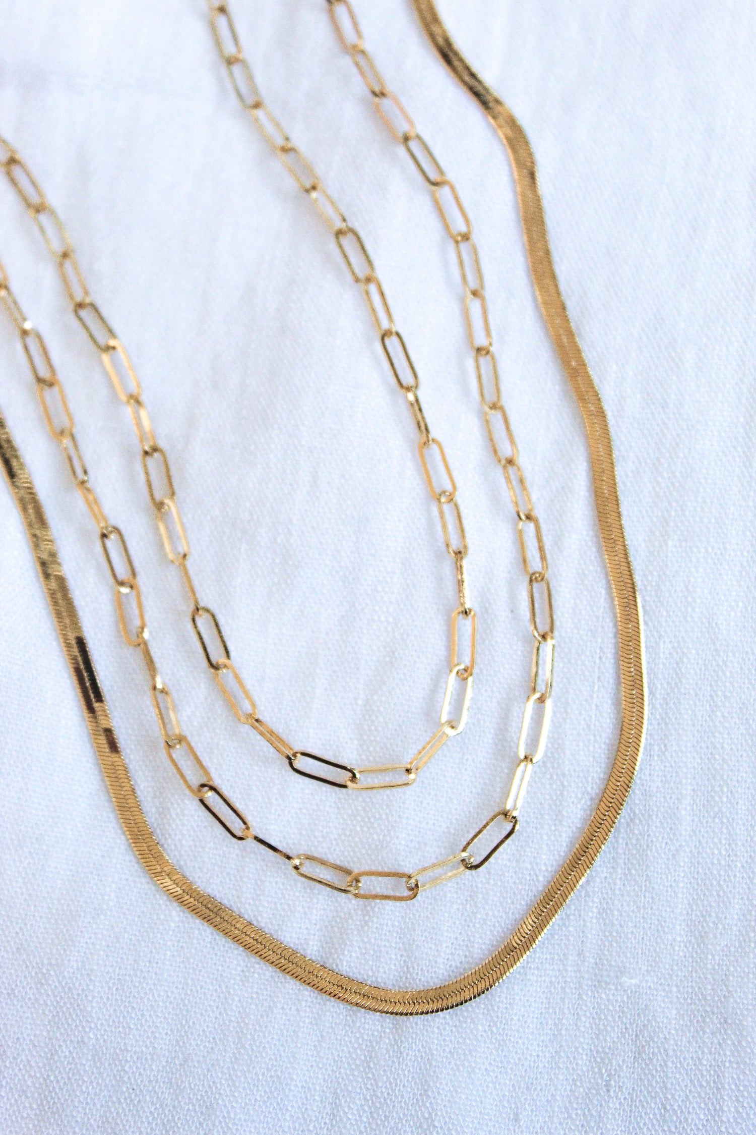 The Wren Chain Layer by Kinsey Designs Archives features three 16k gold plated chains with varying link styles, elegantly layered together and displayed on a white fabric background.