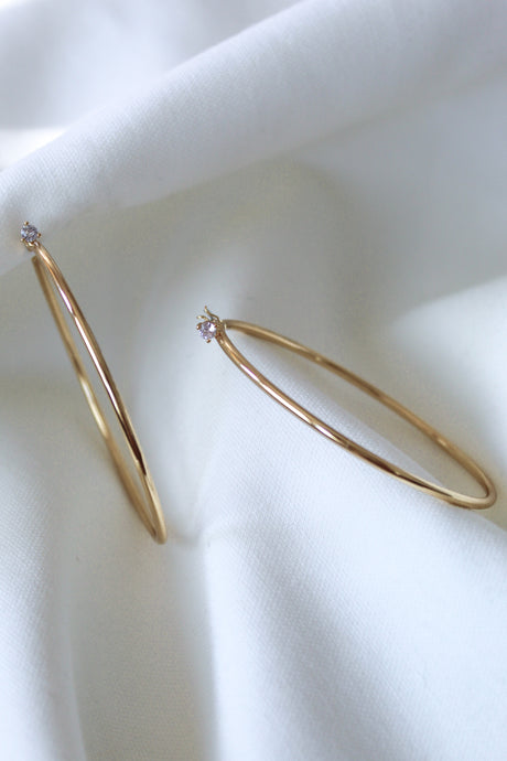 The Xandra Hoop earrings by Kinsey Designs Archives, featuring sparkling cubic zirconia, rest on soft white fabric.