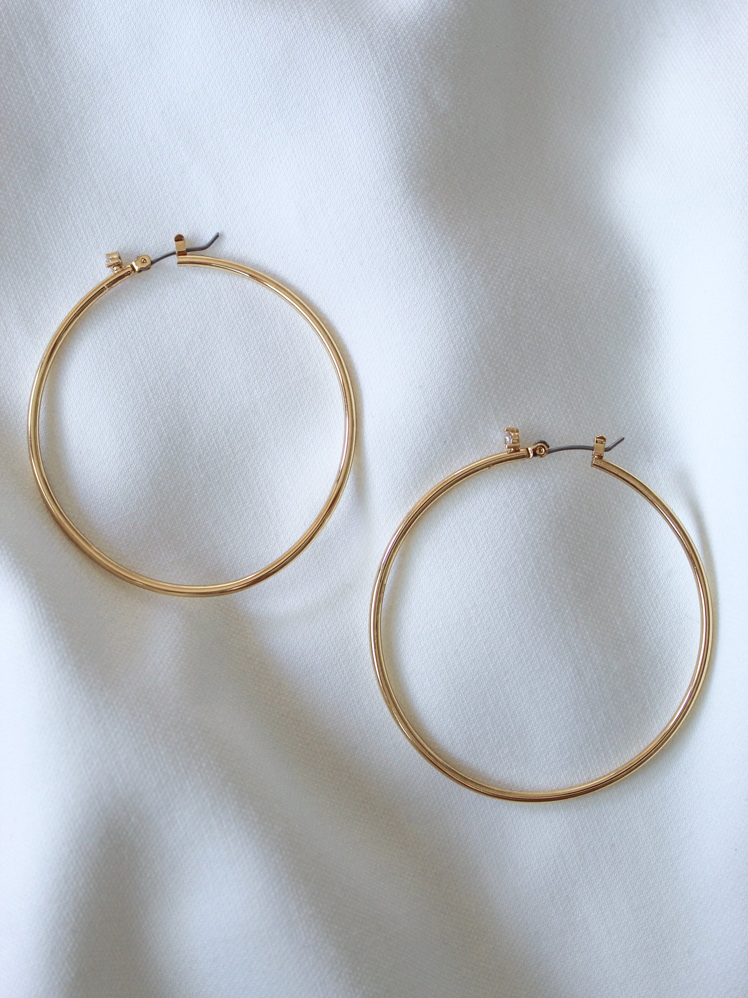 The Xandra Hoop earrings by Kinsey Designs Archives, crafted from gold plated brass, rest elegantly on a soft white fabric background.