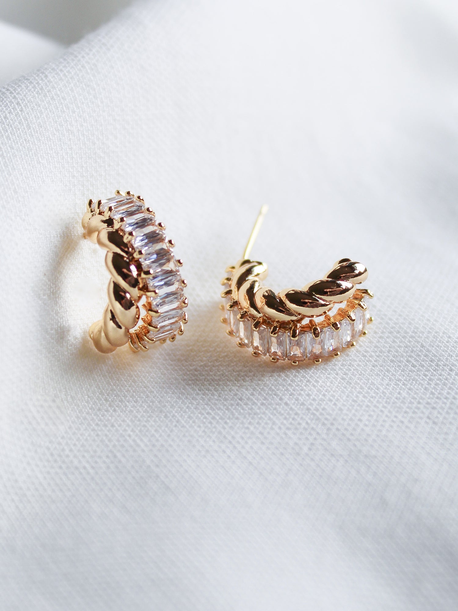 The Zuri Hoop by Kinsey Designs features gold filled earrings accented with clear cubic zirconia, elegantly presented on a soft white fabric background.