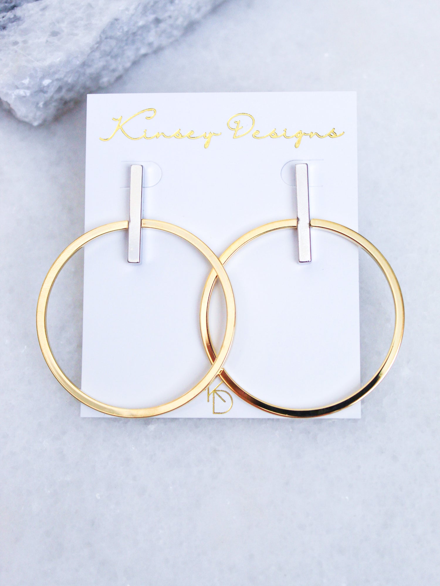 Jocelyn - Mixed Metals gold plated hoop earrings with silver bars (2.5”L x 2”W) by Kinsey Designs Archives, shown on a branded white card atop marble.