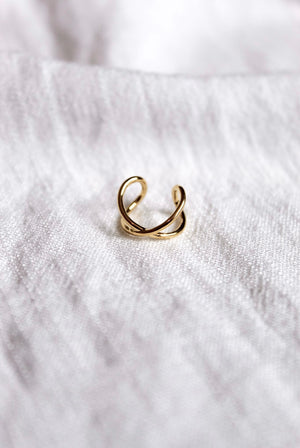 The Criss-Cross Ear Cuff by Kinsey Designs Archives features a delicate gold-plated finish and .5" circumference, showcased on a soft white fabric background.