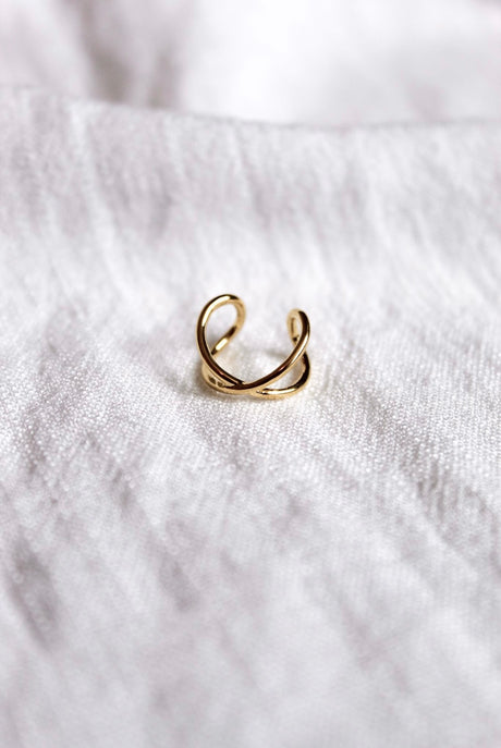 The Criss-Cross Ear Cuff by Kinsey Designs Archives features a delicate gold-plated finish and .5" circumference, showcased on a soft white fabric background.