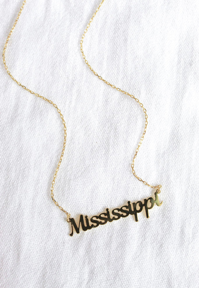 The Kinsey Designs Archives State of Mind Necklace features "Mississippi" in cursive lettering, shown on a white textured fabric background.