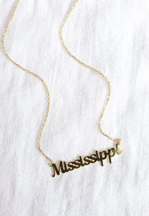 The Kinsey Designs Archives State of Mind Necklace features "Mississippi" in cursive lettering, shown on a white textured fabric background.
