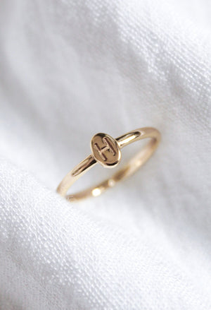 The Kinsey Initial Ring by Kinsey Designs, engraved with an “H,” is shown on textured white fabric—an elegant, personalized jewelry piece ideal for daily wear.