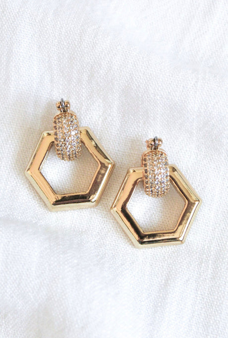 The Stevie 2-Way Hoop by Kinsey Designs Archives features gold-plated huggie earrings with removable hexagon drops and cubic zirconia accents, shown on a white fabric background.