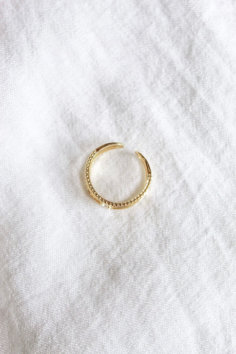 The Madi Ring by Kinsey Designs Archives, a gold-plated adjustable open ring with delicate details, rests on a white textured fabric background.