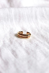 The Blurred Lines Ear Cuff by Kinsey Designs Archives features a gold-plated double band design, measuring .75” wide, shown resting on soft white textured fabric.