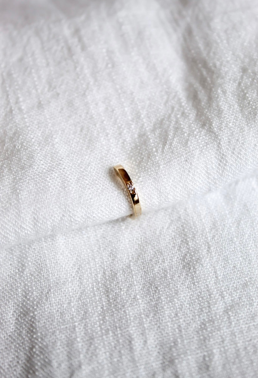 The Leni Ear Cuff by Kinsey Designs Archives, gold plated with a small cubic zirconia, rests on textured white fabric, adding understated elegance to your jewelry collection.