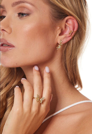 A woman wears butterfly jewelry: gold earrings, an ear cuff, and the Kinsey Designs Archives Willow Butterfly Ring—a gold-filled piece—paired with natural makeup and manicured nails.