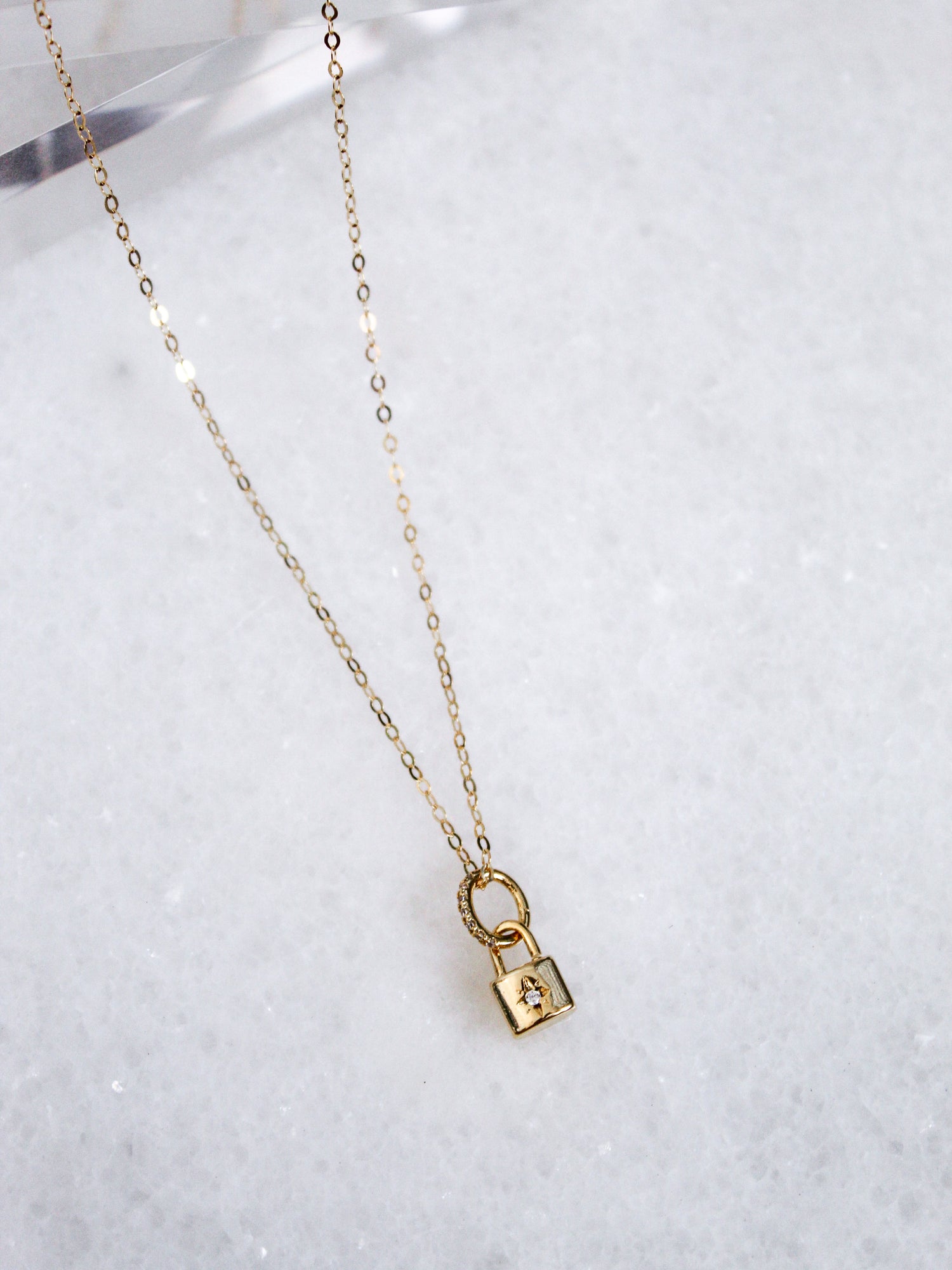 The Blaire Lock Necklace by Kinsey Designs Archives features a small gold-plated brass padlock charm on a 16k gold-filled chain, elegantly displayed on white marble.