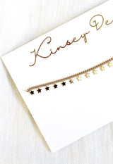 The Starry Choker by Kinsey Designs Archives features a gold plated chain with delicate star charms, displayed on a white "Kinsey D" card—a stylish, elegant addition to your jewelry collection.