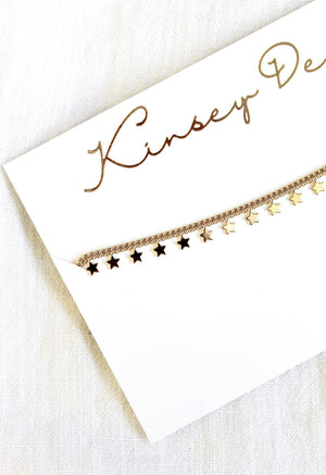 The Starry Choker by Kinsey Designs Archives features a gold plated chain with delicate star charms, displayed on a white "Kinsey D" card—a stylish, elegant addition to your jewelry collection.