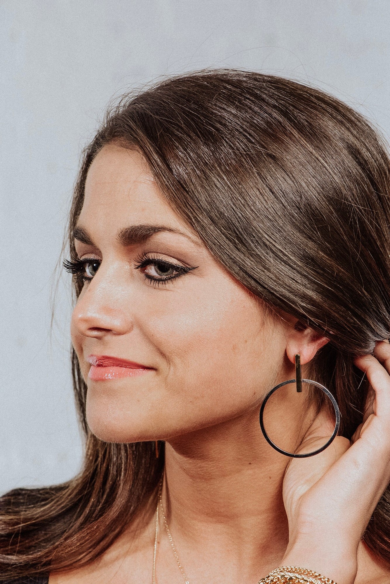 Woman with long brown hair, subtle makeup, and a slight smile looks left wearing Kinsey Designs Archives’ Jocelyn - Mixed Metals gold plated hoop earrings (2.5” long, 2” wide).