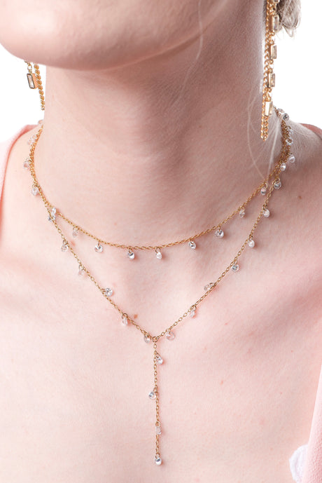 The Clare Lariat by Kinsey Designs Archives is an 18k gold plated necklace with small clear CZ charms and an adjustable extender, shown on a fair-skinned model.
