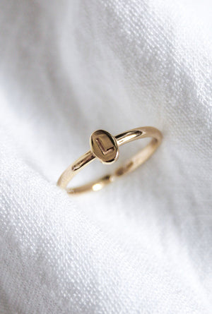 The Kinsey Initial Ring by Kinsey Designs, engraved with the letter "L," rests on a soft white fabric background, making it a stunning piece of personalized jewelry.