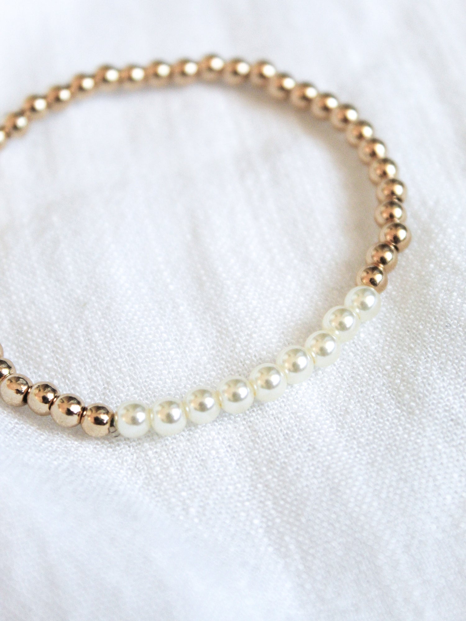 The Liam Stacking Bracelet by Kinsey Designs features gold filled and white pearl beads in an adjustable stretch design, shown on a white fabric background. Available in multiple sizes.